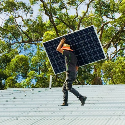 man carrying solar panel across roof wearing a hat